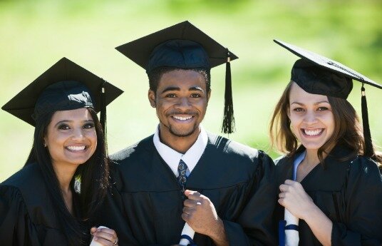 Three smiling students at graduation wearing caps and gowns